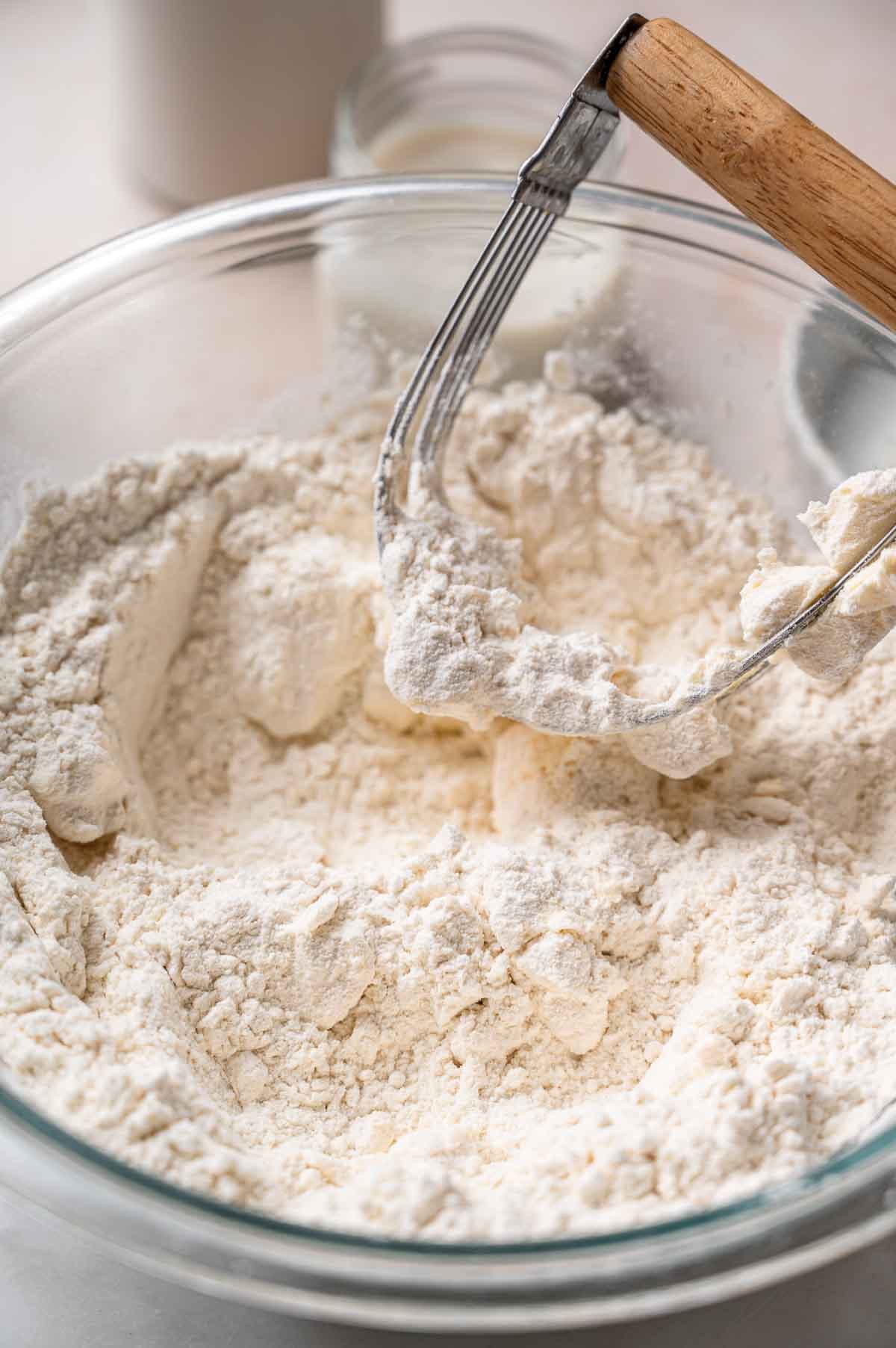 a pastry cutter resting on the edge of a large bowl filled with crumbly flour and butter.