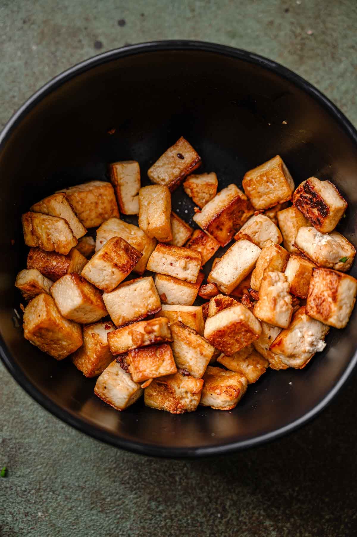 a close up of the panfried tofu in a dark bowl.