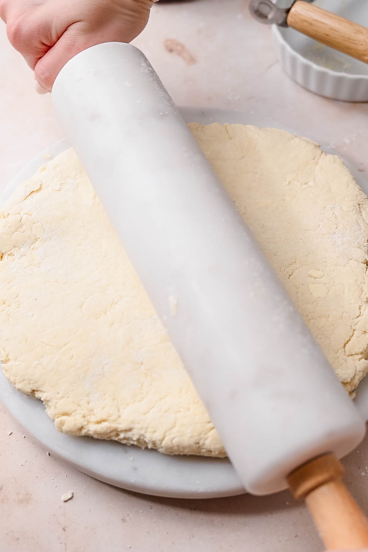 two hands using a white marble rolling pin to roll out biscuit dough.