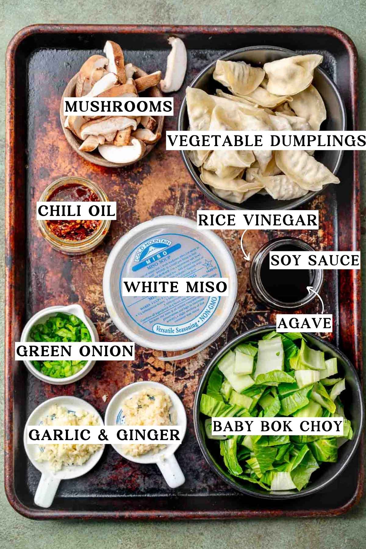 ingredients like soup dumplings, mushrooms, green onions, bok choy and miso on a metal baking sheet.