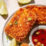 a slab of crispy panfried panko coated tofu with green onions and lime wedges.