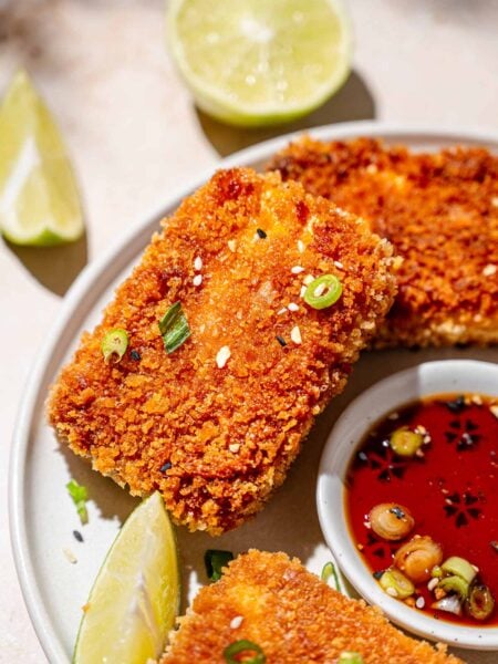 a slab of crispy panfried panko coated tofu with green onions and lime wedges.