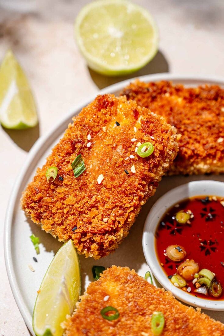 a slab of crispy panfried panko coated tofu with green onions and lime wedges.