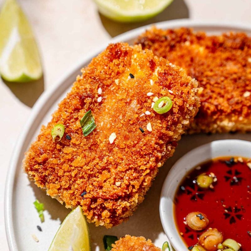 a slab of crispy panfried panko coated tofu with green onions and lime wedges.
