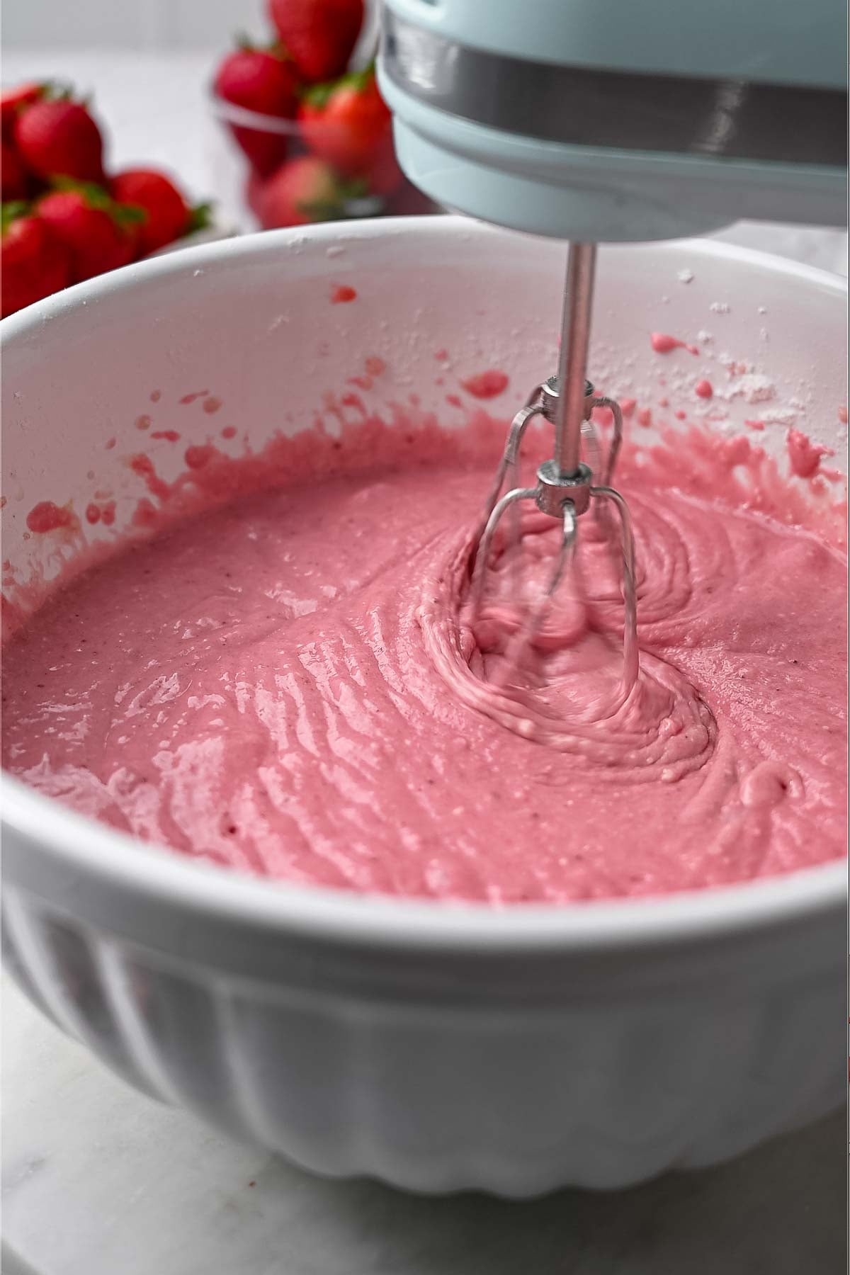 hand mixers mixing the eggless strawberry cake batter in a large white bowl.