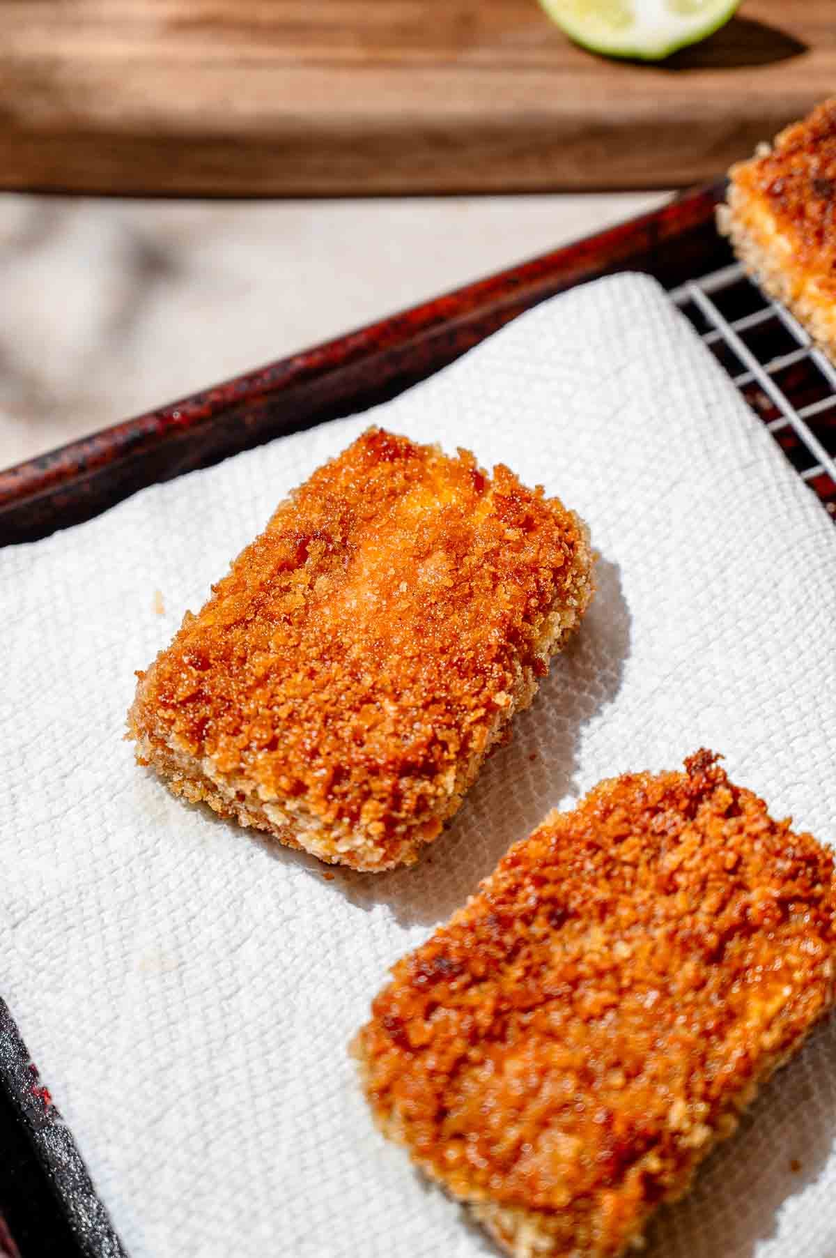 two slabs of golden brown fried panko tofu on paper towels.