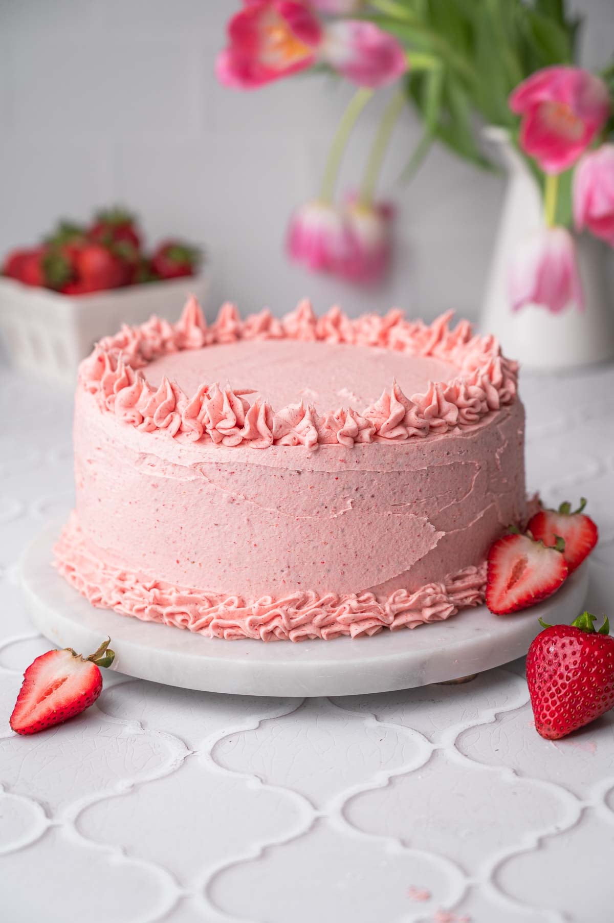 the frosted strawberry layer cake on a marble stand.