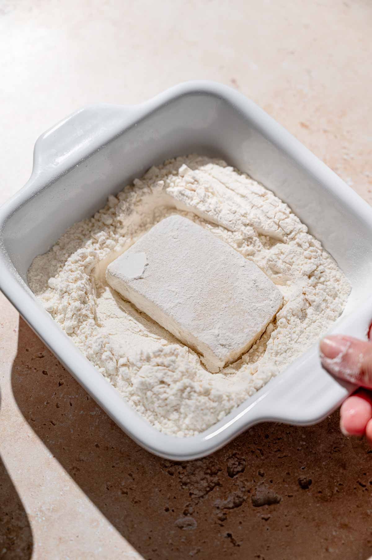 a slab of tofu in a dish with flour.