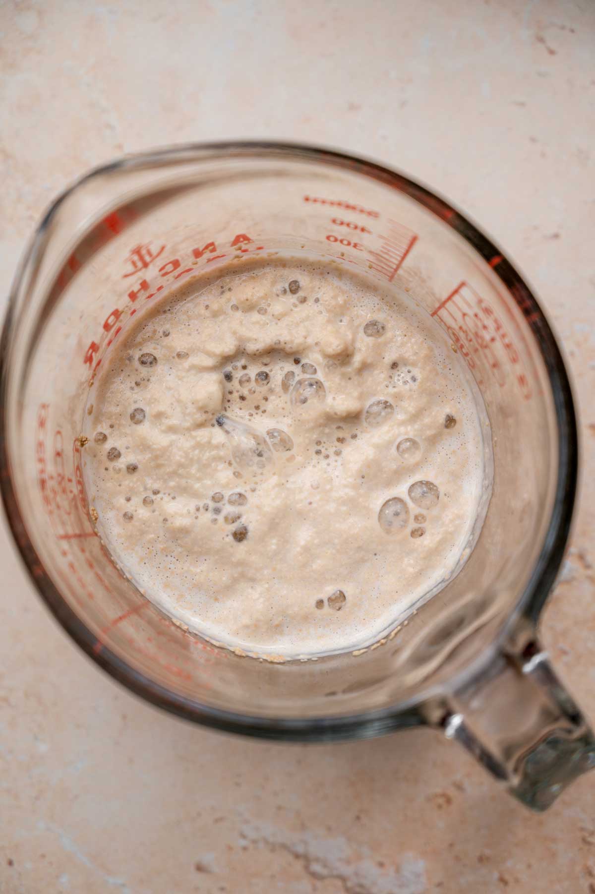 yeast frothed up in a glass measuring cup with soy milk.
