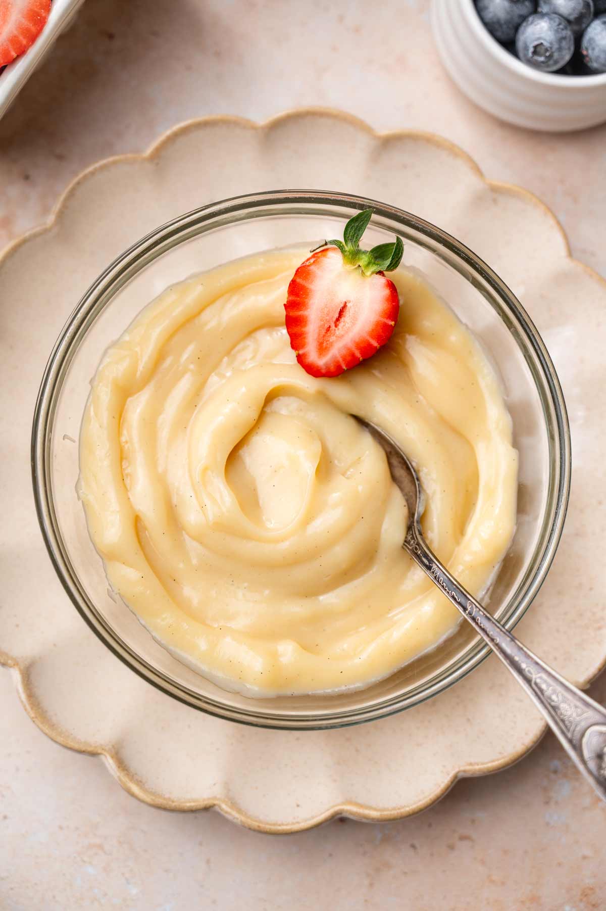 a bowl of vegan vanilla custard with a sliced strawberry and a spoon.