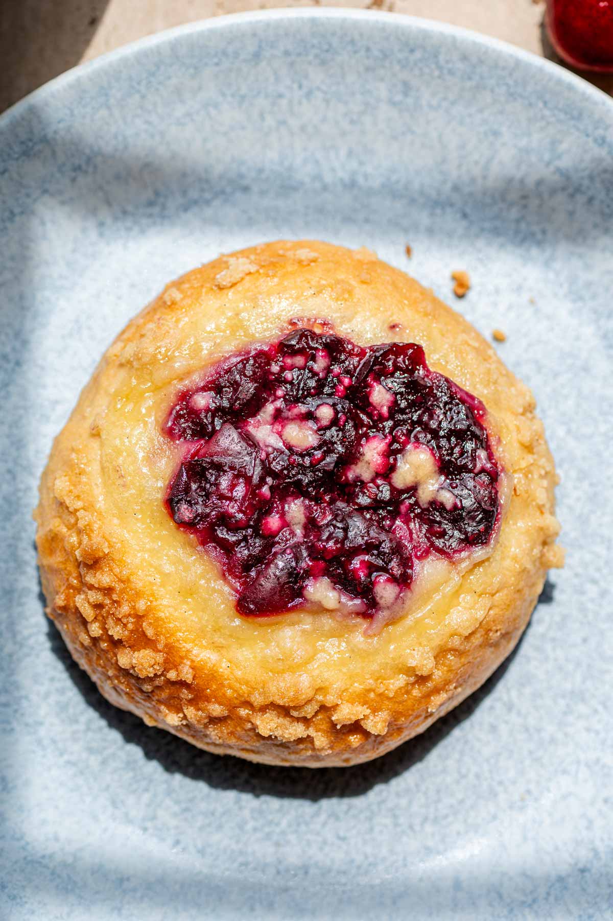 a brioche custard bun with cherries on a blue plate.