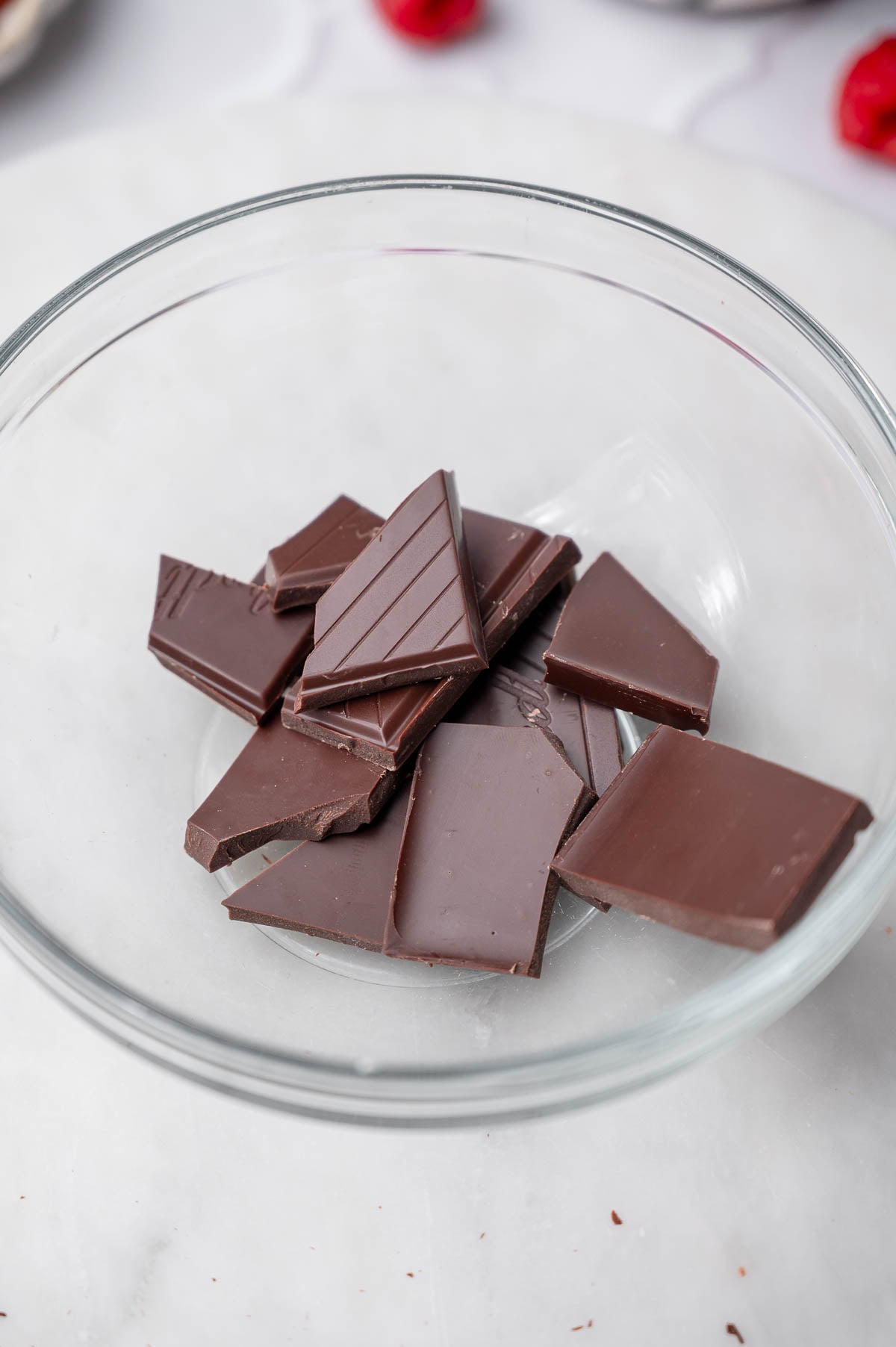 Chopped dark chocolate in a glass bowl before melting for tofu chocolate mousse.