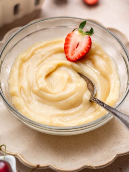 a bowl of vegan vanilla custard with a sliced strawberry and a spoon.
