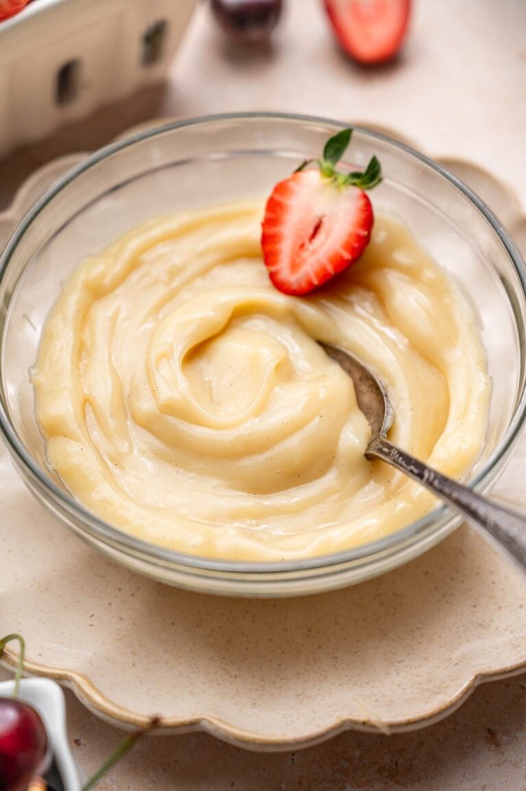 a bowl of vegan vanilla custard with a sliced strawberry and a spoon.