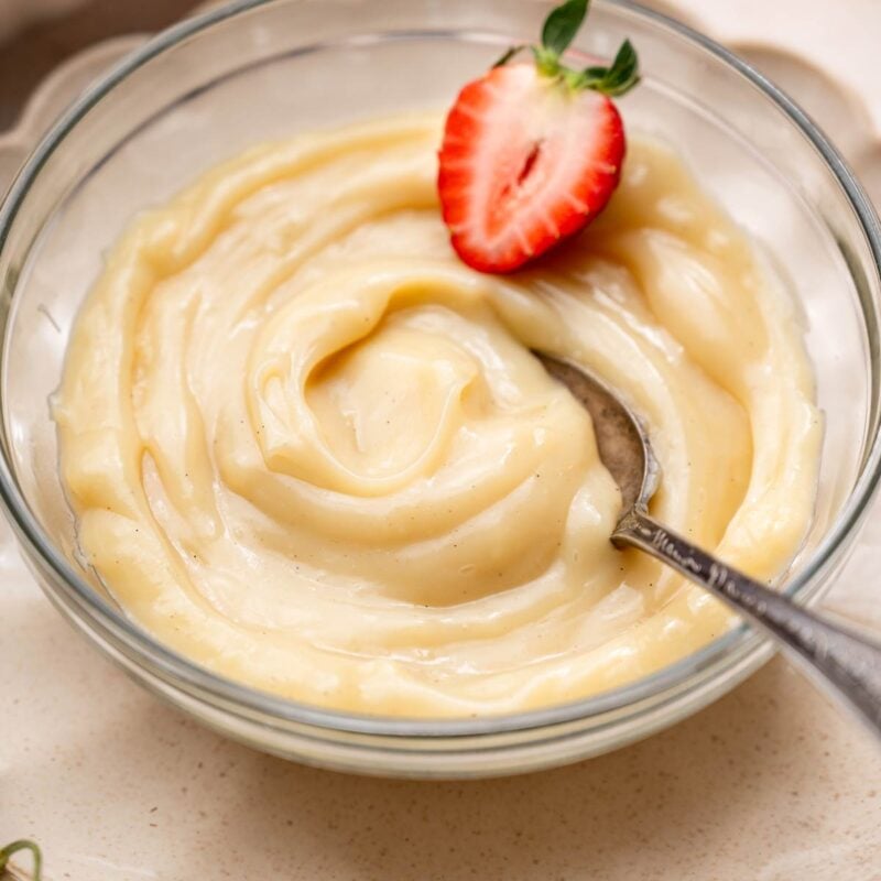 a bowl of vegan vanilla custard with a sliced strawberry and a spoon.