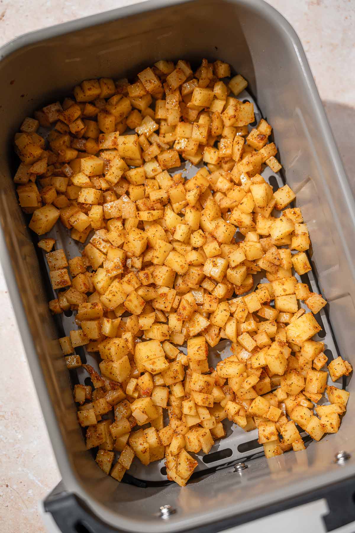 Diced potatoes spread in an air fryer basket before cooking.