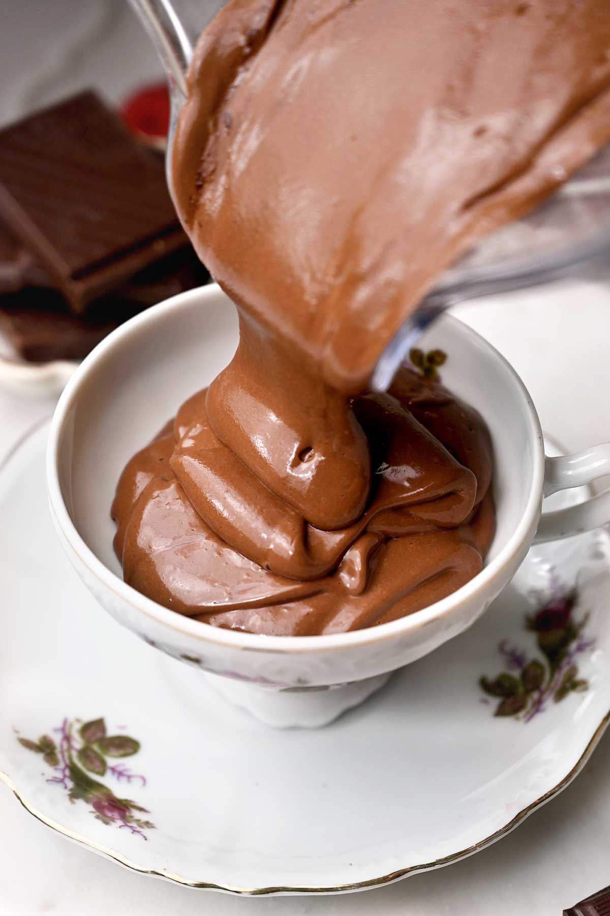 Vegan chocolate mousse being poured into a teacup before chilling until thick and creamy.