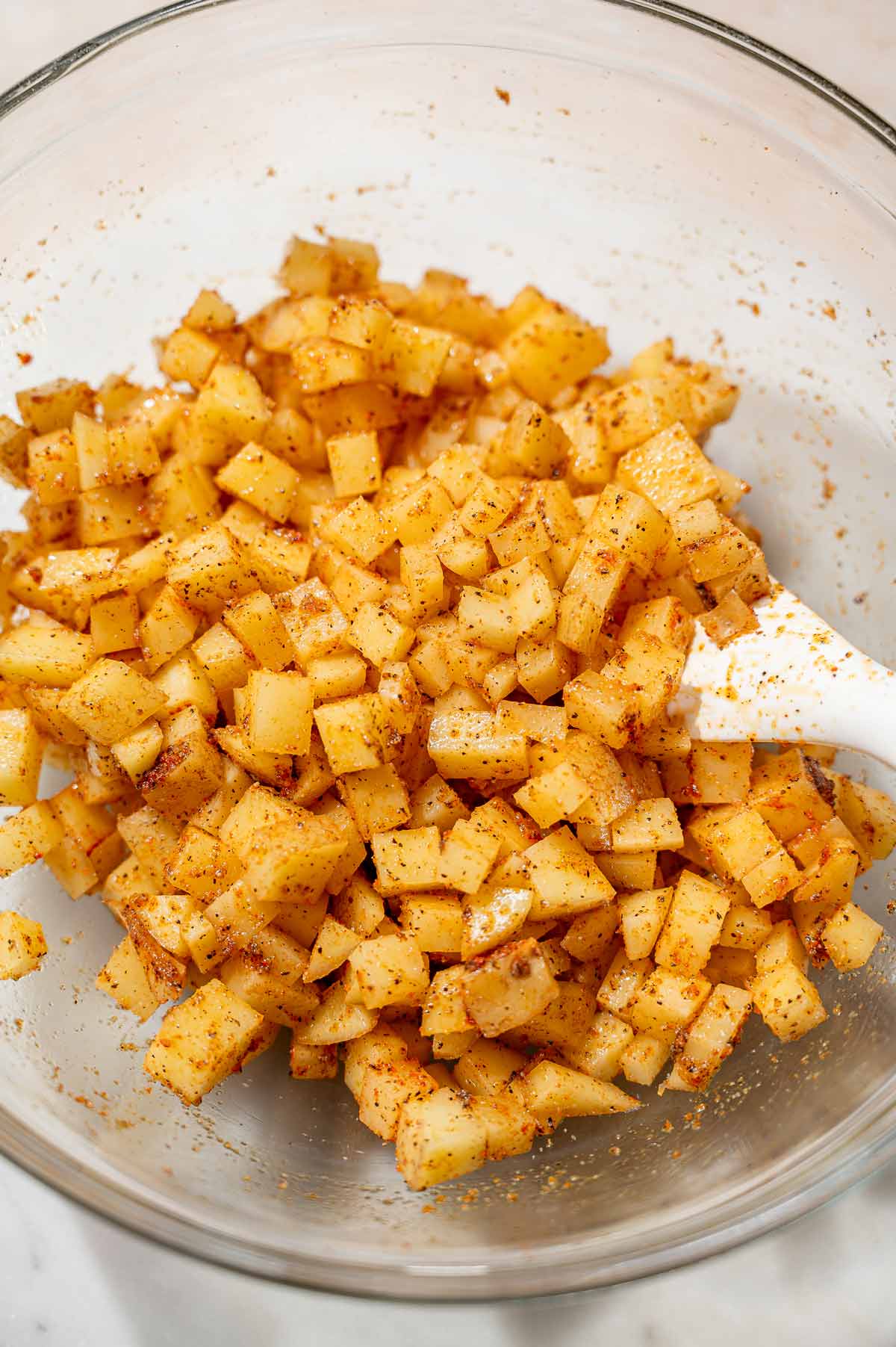 Diced potatoes tossed with oil and spices in a glass bowl.