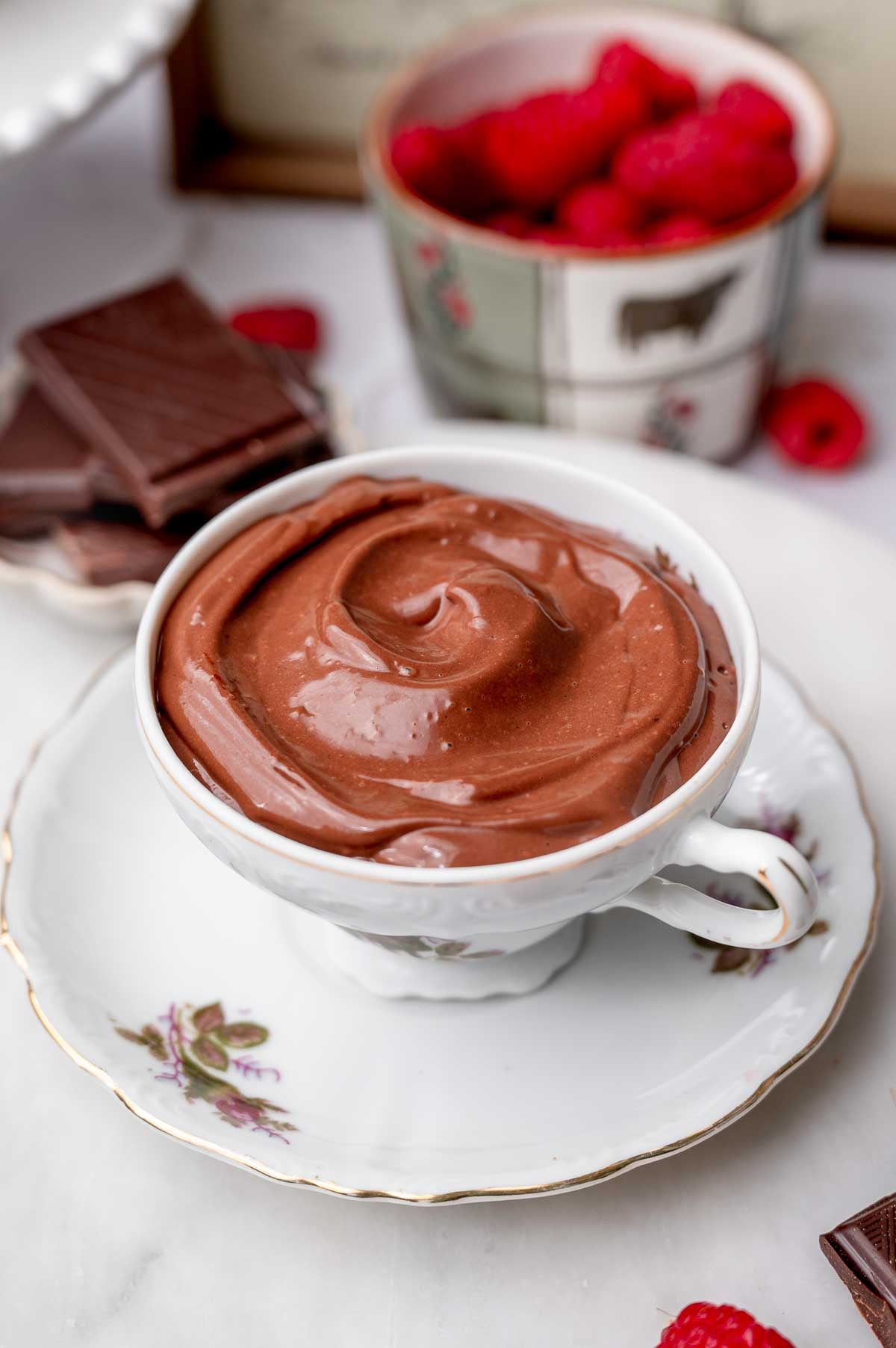 Smooth chocolate mousse served in a small teacup with raspberries and dark chocolate.