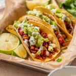 Vegan chorizo tacos with potato, guacamole, cilantro lime crema, scallions, and lime wedges.