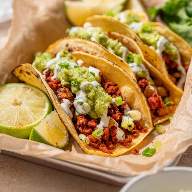 Vegan chorizo tacos with potato, guacamole, cilantro lime crema, scallions, and lime wedges.