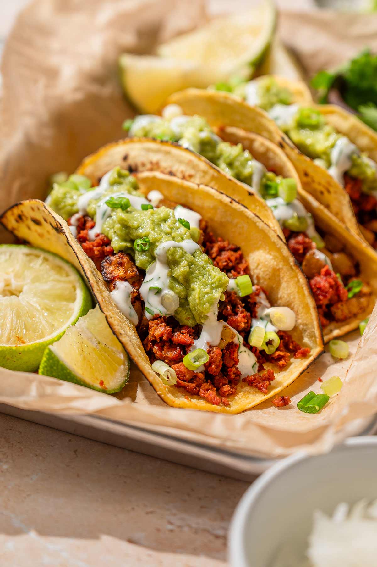Vegan chorizo tacos with potato, guacamole, cilantro lime crema, scallions, and lime wedges.