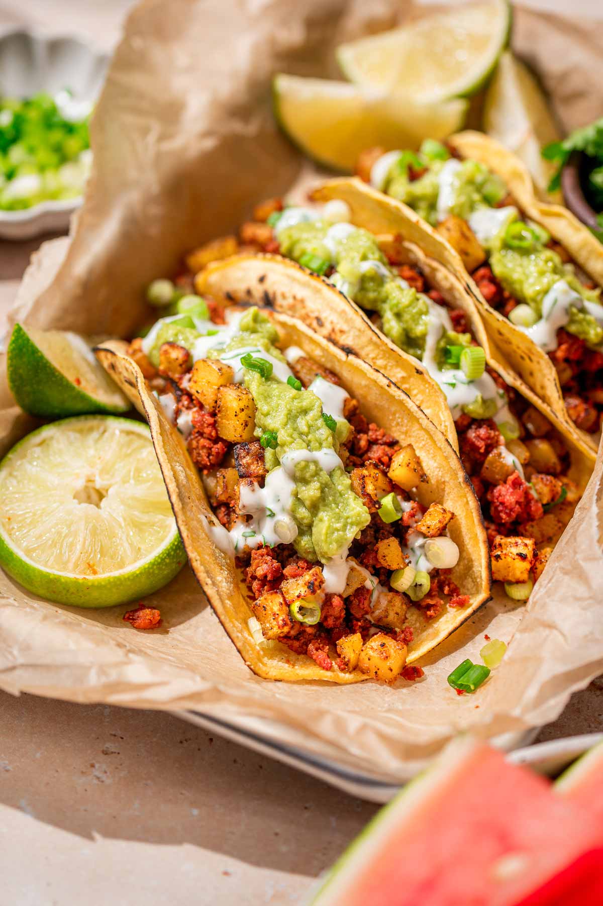 Weeknight vegan chorizo tacos with crispy potatoes, guacamole, cilantro crema, lime, and watermelon.
