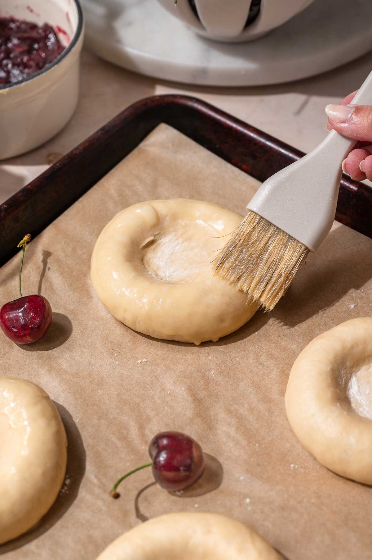 a hand brushing the shaped bun with vegan egg wash.