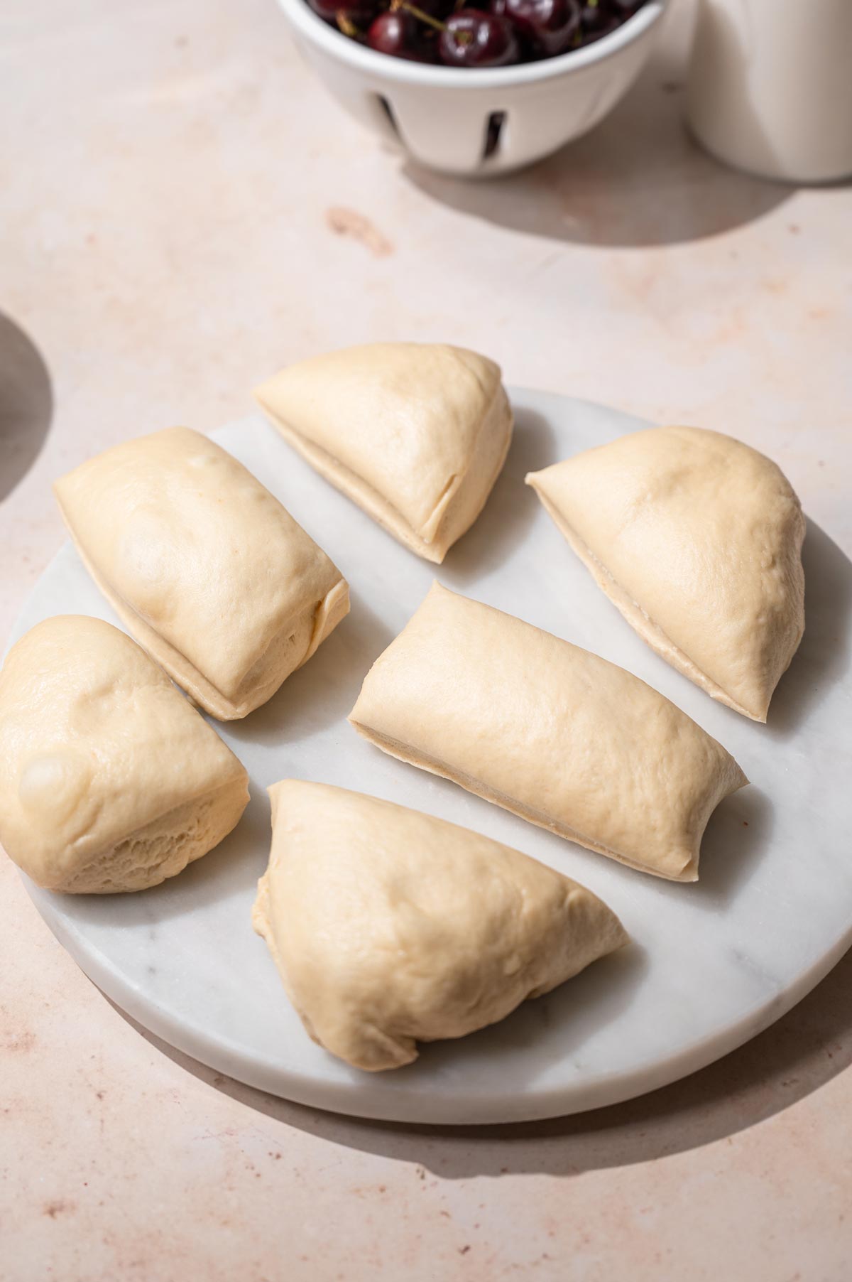 brioche dough cut into six pieces on a marble cutting board.