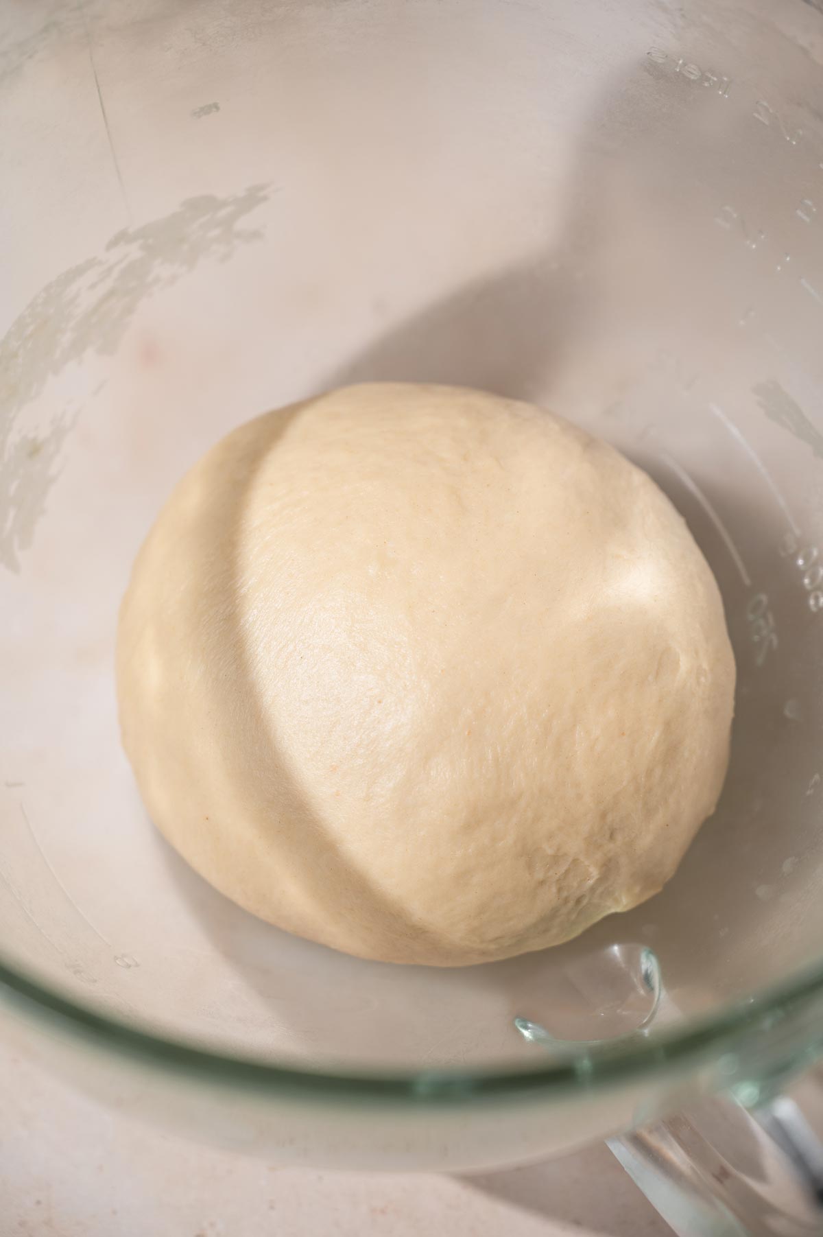 a smooth ball of kneaded vegan brioche dough in a glass stand mixer bowl.
