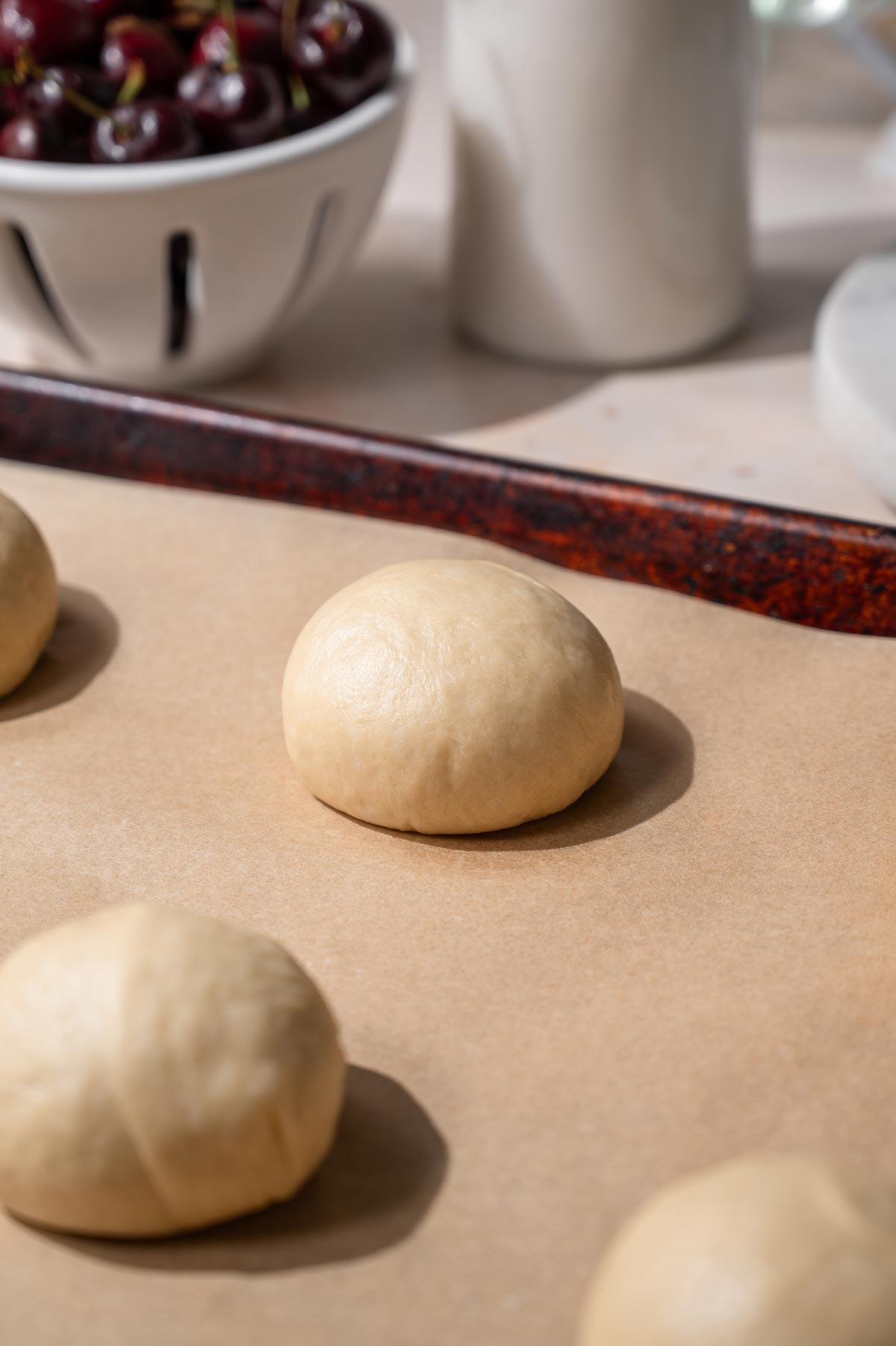 eggless brioche dough rolled into a smooth ball on a parchment lined baking sheet.