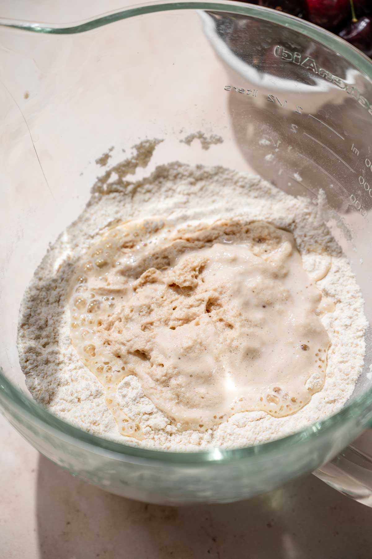 dry ingredients with frothy yeast mixture in a glass stand mixer bowl.