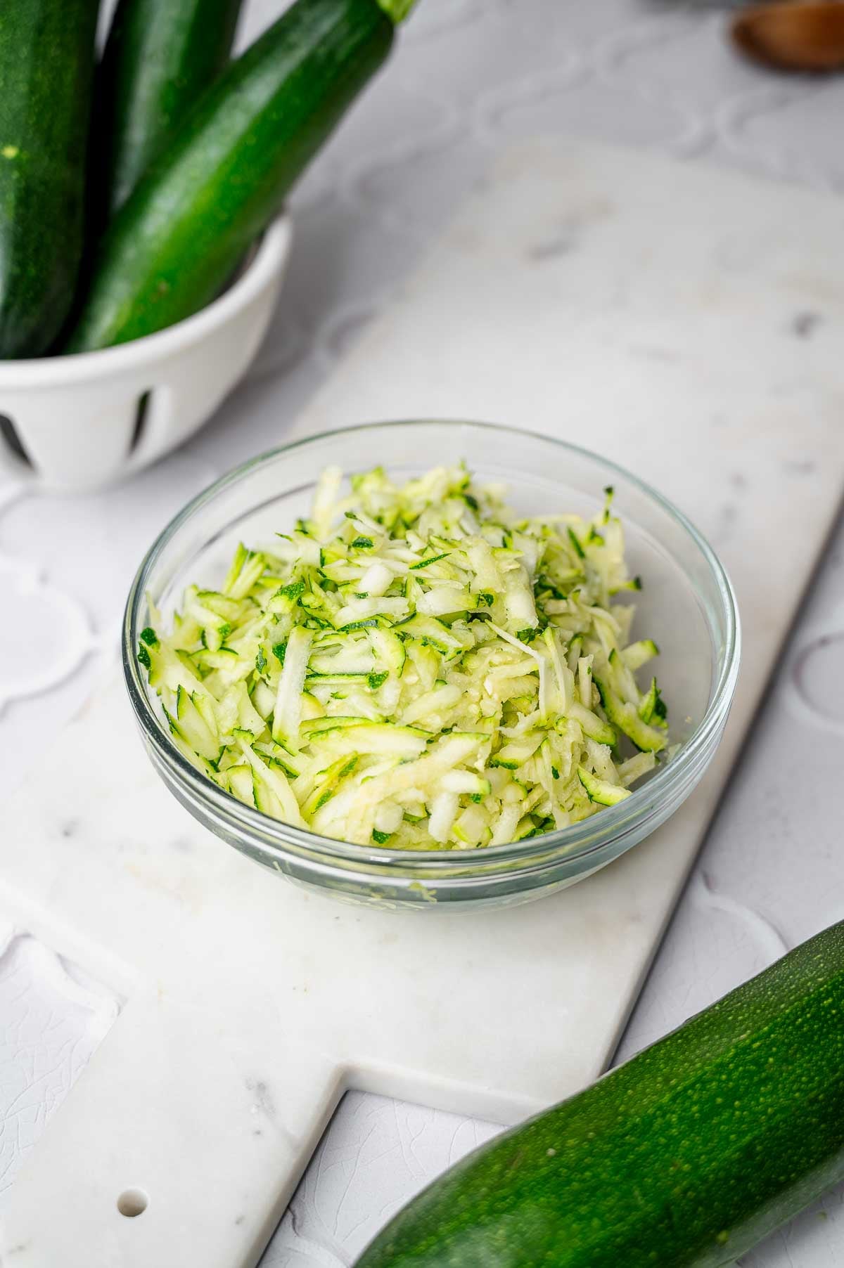 Freshly shredded zucchini in a glass bowl for making vegan zucchini bread.