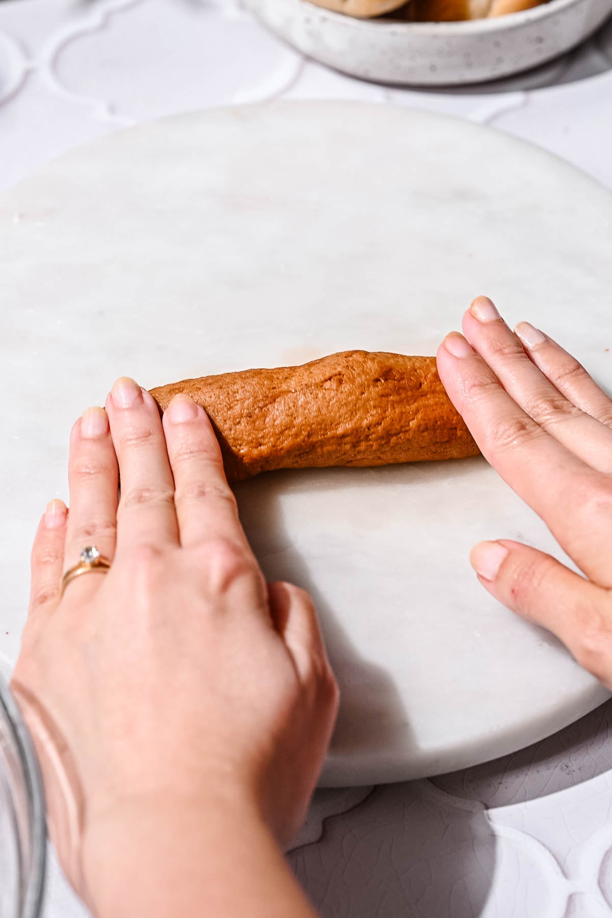 Hands rolling vegan hot dog dough into a smooth sausage shape.