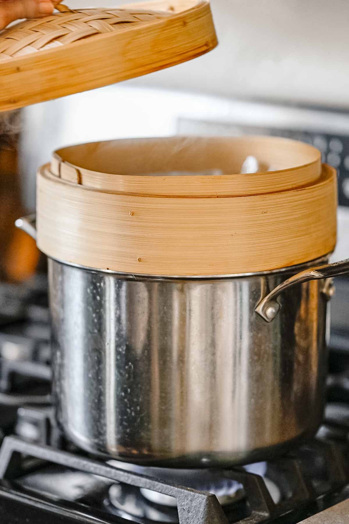Bamboo steamer over a pot on the stovetop with steam rising for cooking vegan hot dogs.