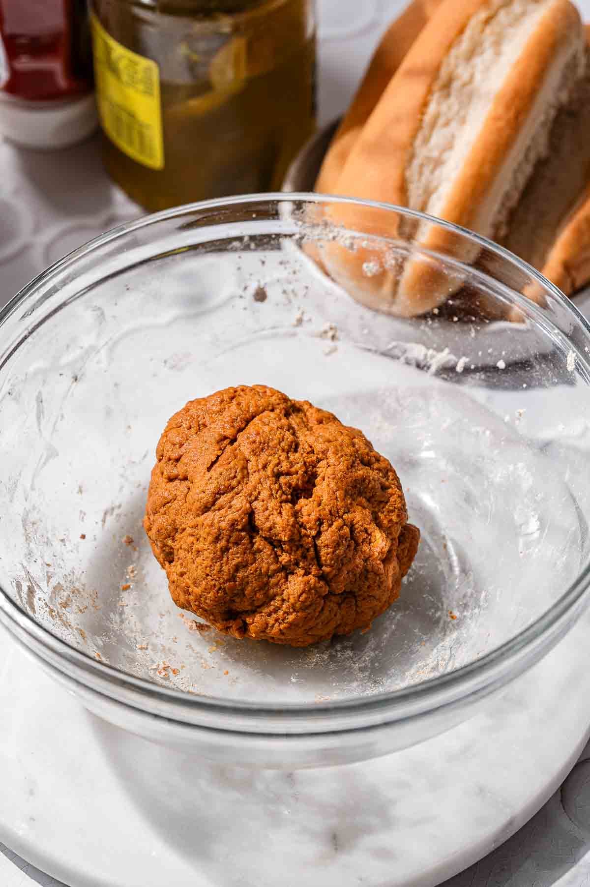 Ball of seitan dough resting in a glass mixing bowl.
