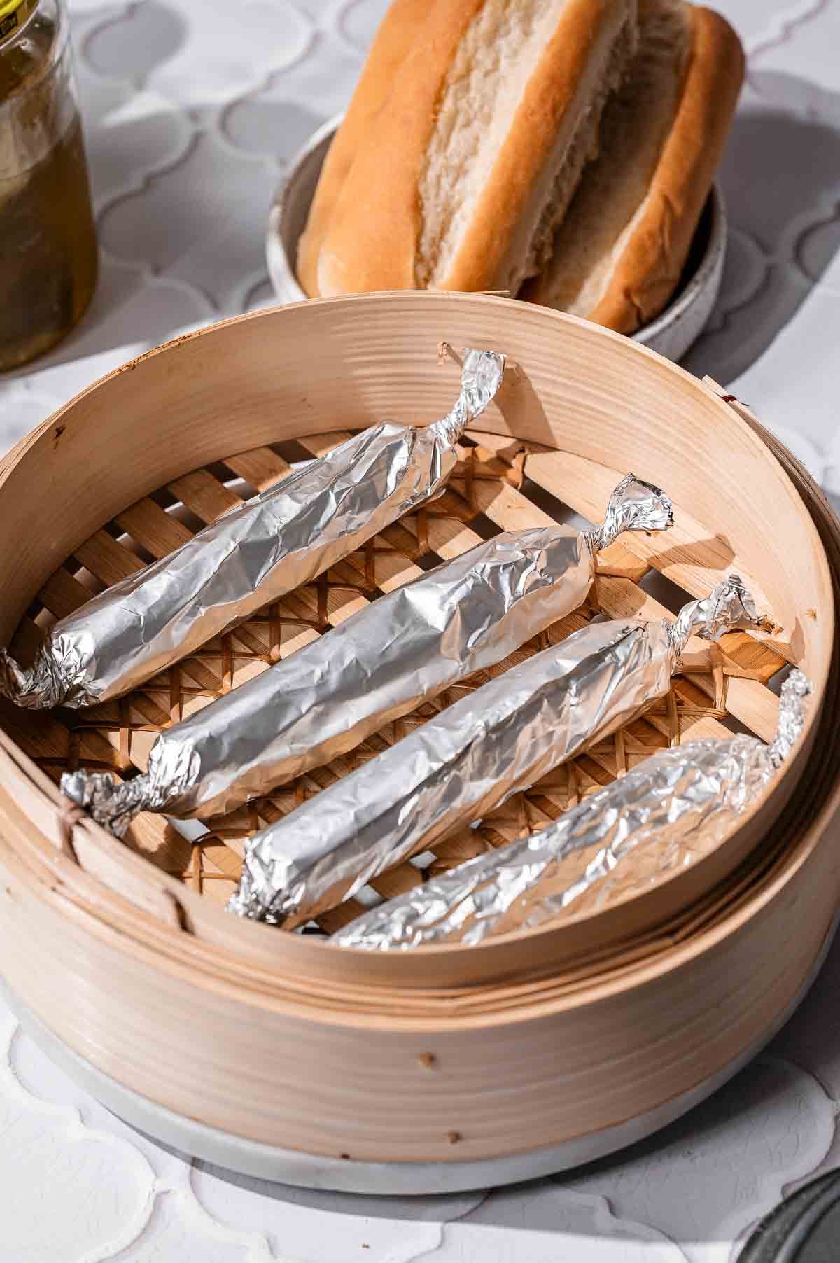 Foil-wrapped vegan hot dogs arranged inside a bamboo steamer basket.