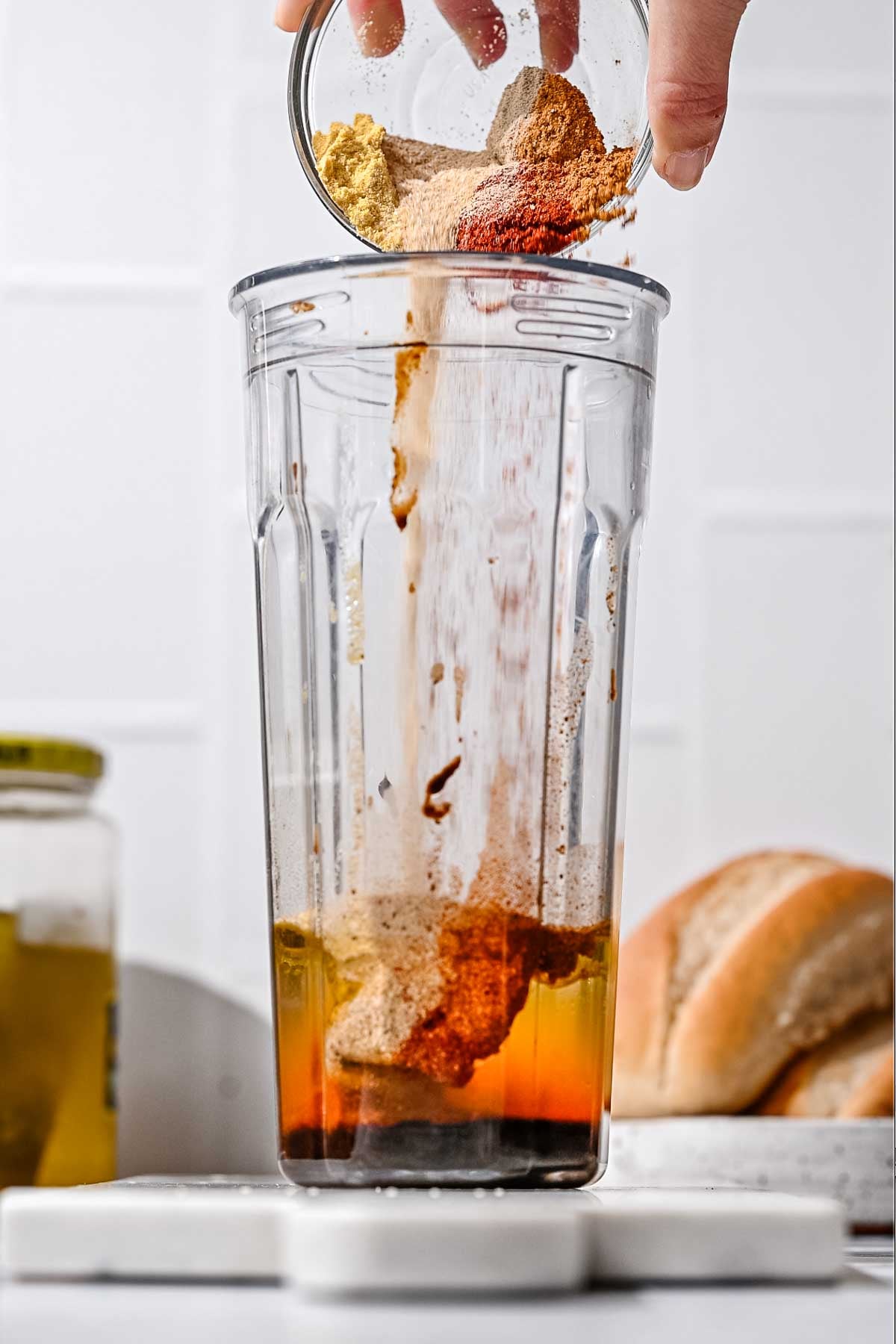 A blend of spices being poured into a blender cup with oil and liquid ingredients.