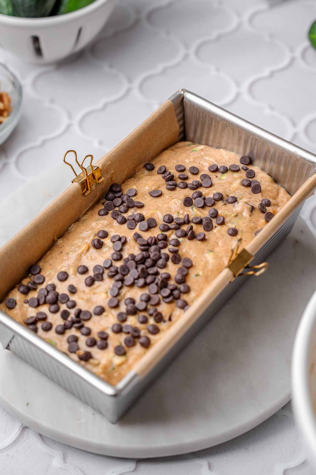 Vegan zucchini bread batter in a parchment-lined loaf pan topped with chocolate chips before baking.
