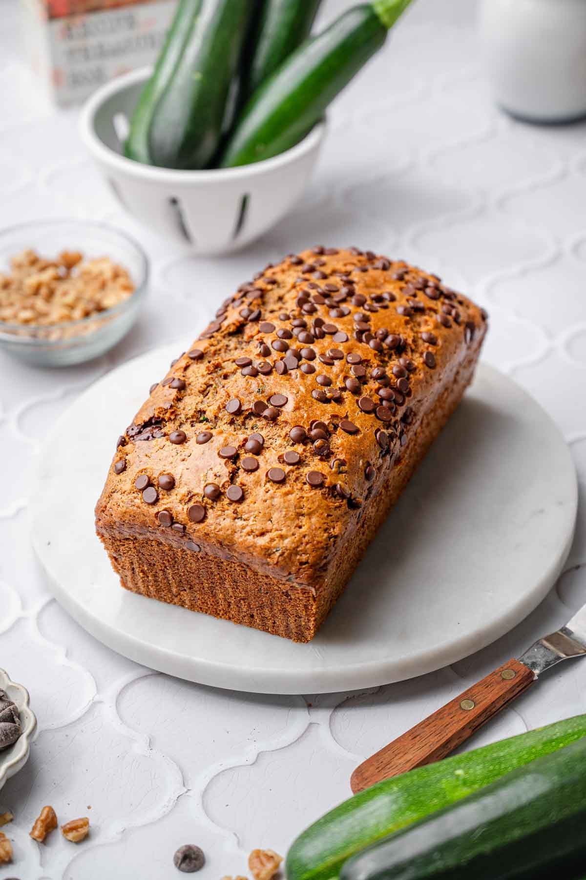 Whole loaf of vegan zucchini bread topped with chocolate chips on a white serving board.