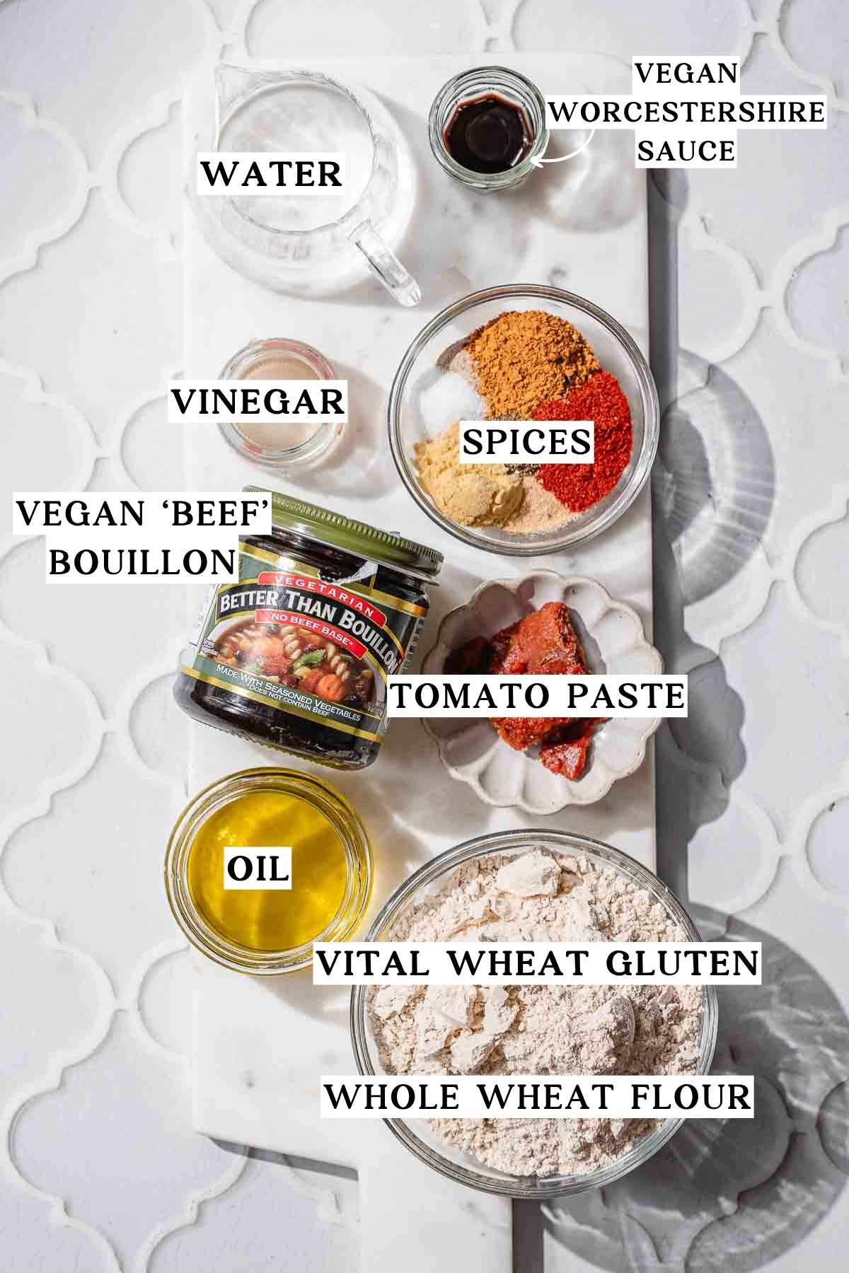 Labeled ingredients for vegan hot dogs arranged on a white board, including vital wheat gluten, oil, tomato paste, spices, Worcestershire sauce, vinegar, water, and vegan beef bouillon.