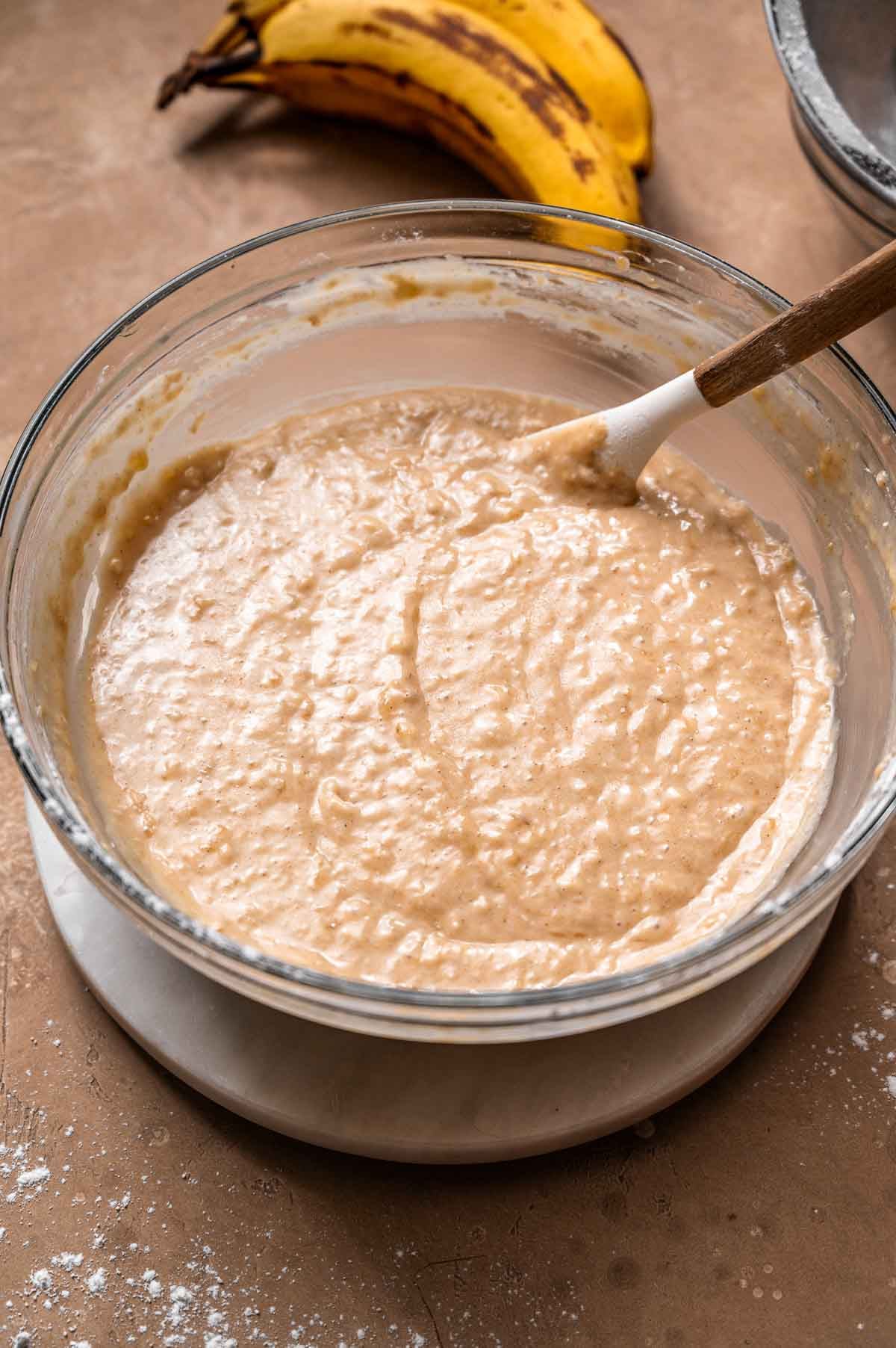 Thick banana cake batter in a glass bowl.