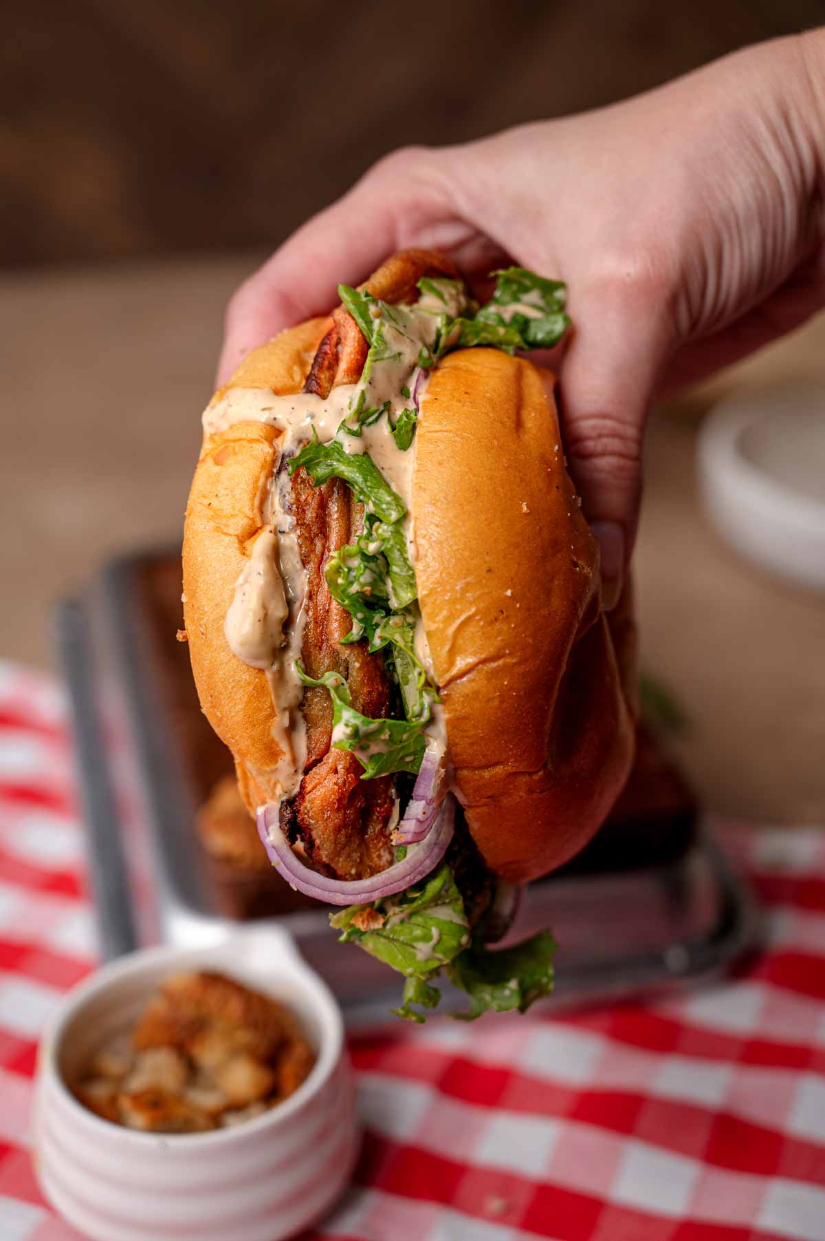 a hand holding a baked vegan chicken caesar sandwich.