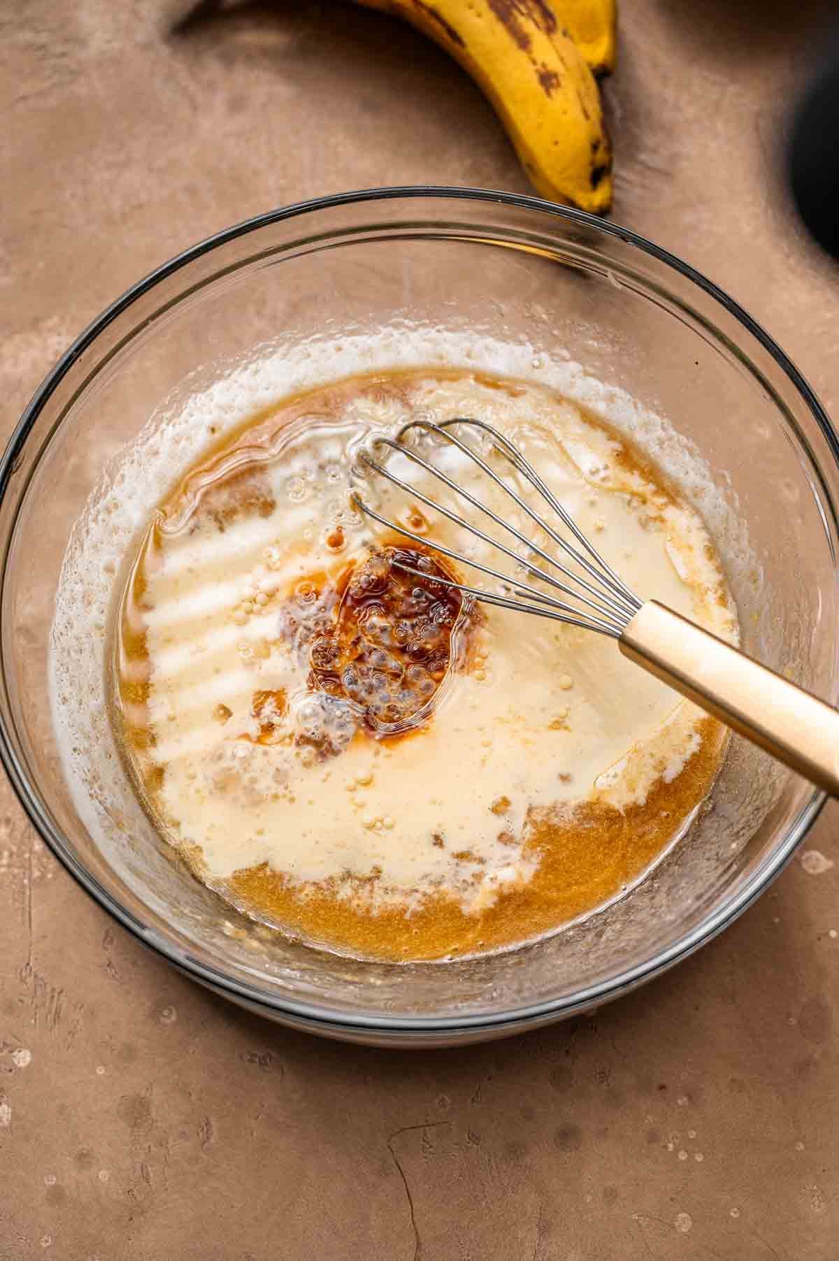 banana cake wet ingredients in a glass bowl with a whisk, ready to be mixed.
