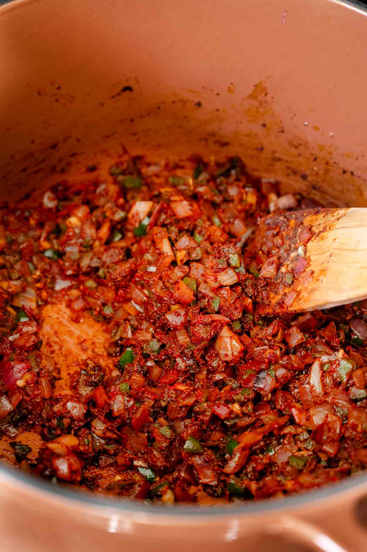Chili spices mixed in with aromatics in a brown Dutch oven.