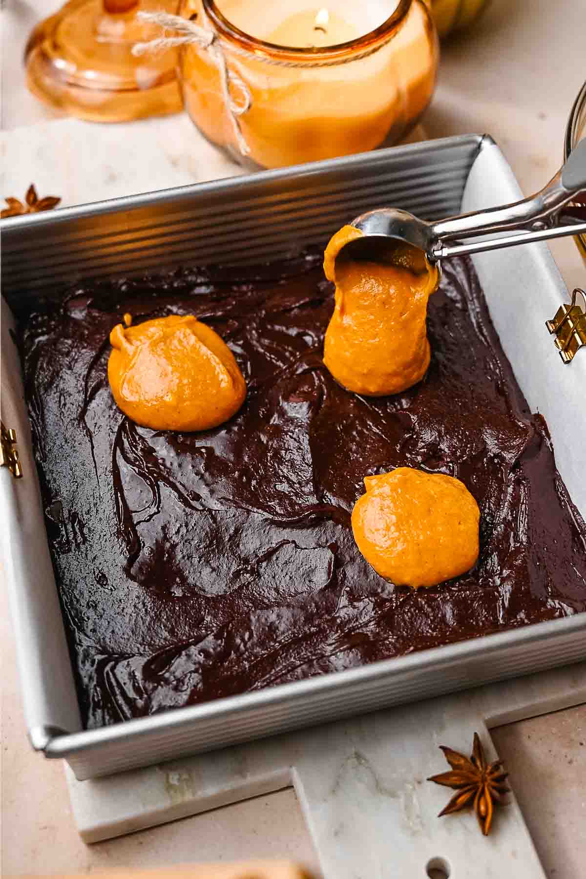 the brownie batter in a metal pan with dollops of pumpkin on top.