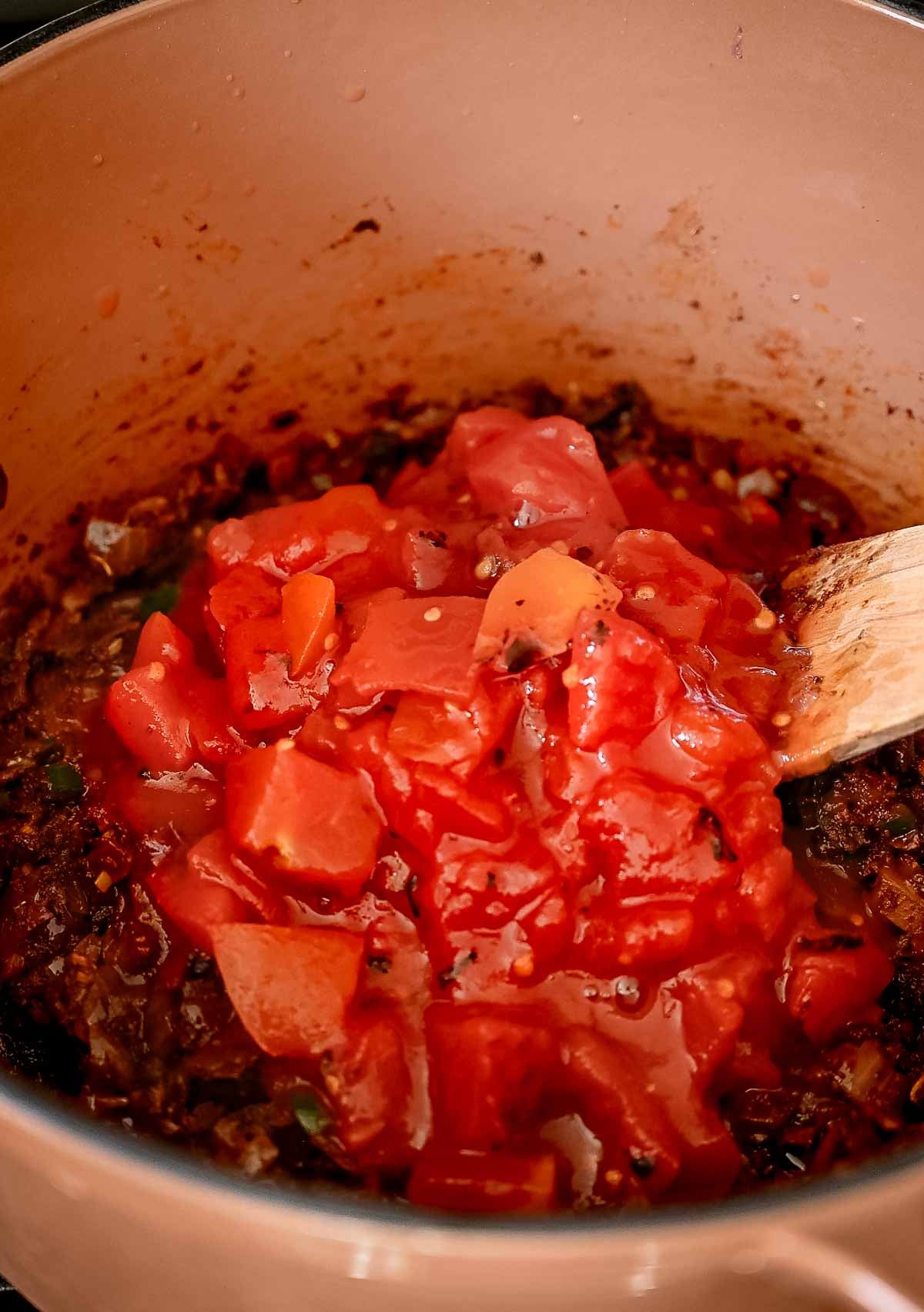 Fire roasted tomatoes added on top of the spiced aromatics in a brown Dutch oven.