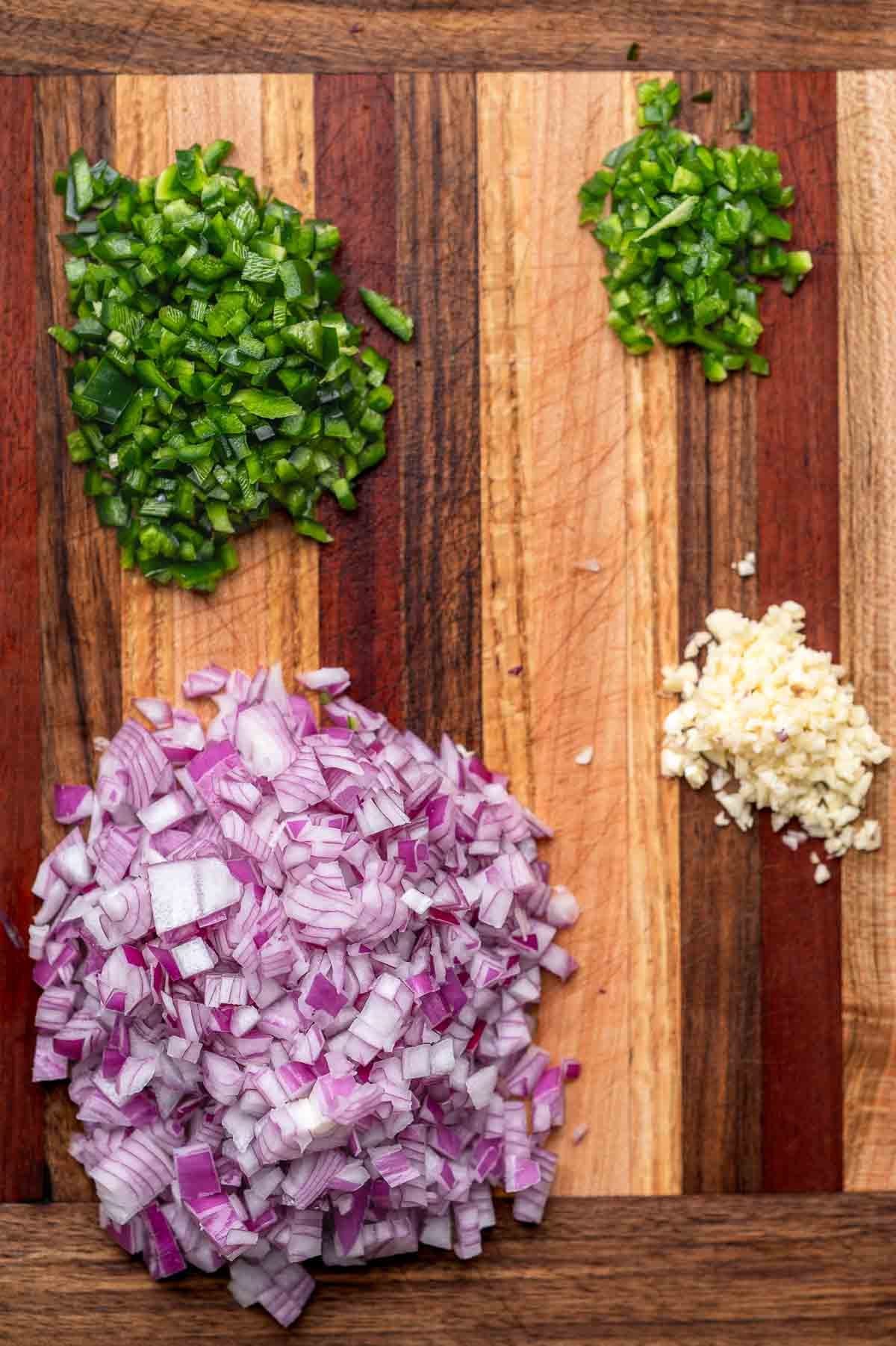 red onion, garlic, poblano pepper, and jalapeno diced small on a wood cutting board.