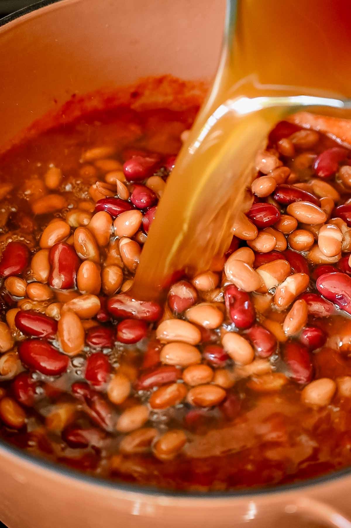 Red kidney beans, pinto beans and vegetarian beef broth being poured into a large Dutch oven to make Vegan chili.