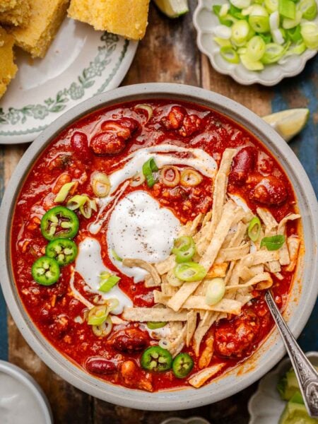 a bowl of vegan chili with kidney beans and vegetarian tvp beef topped with dairy-free sour cream, green onions and tortilla strips.